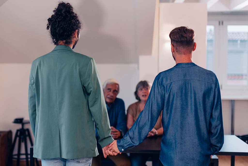 gay couple holding hands coming out to an older parent couple