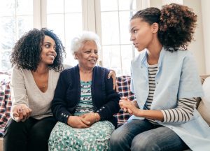 Black female social worker talking with two black women, one younger and one, older.