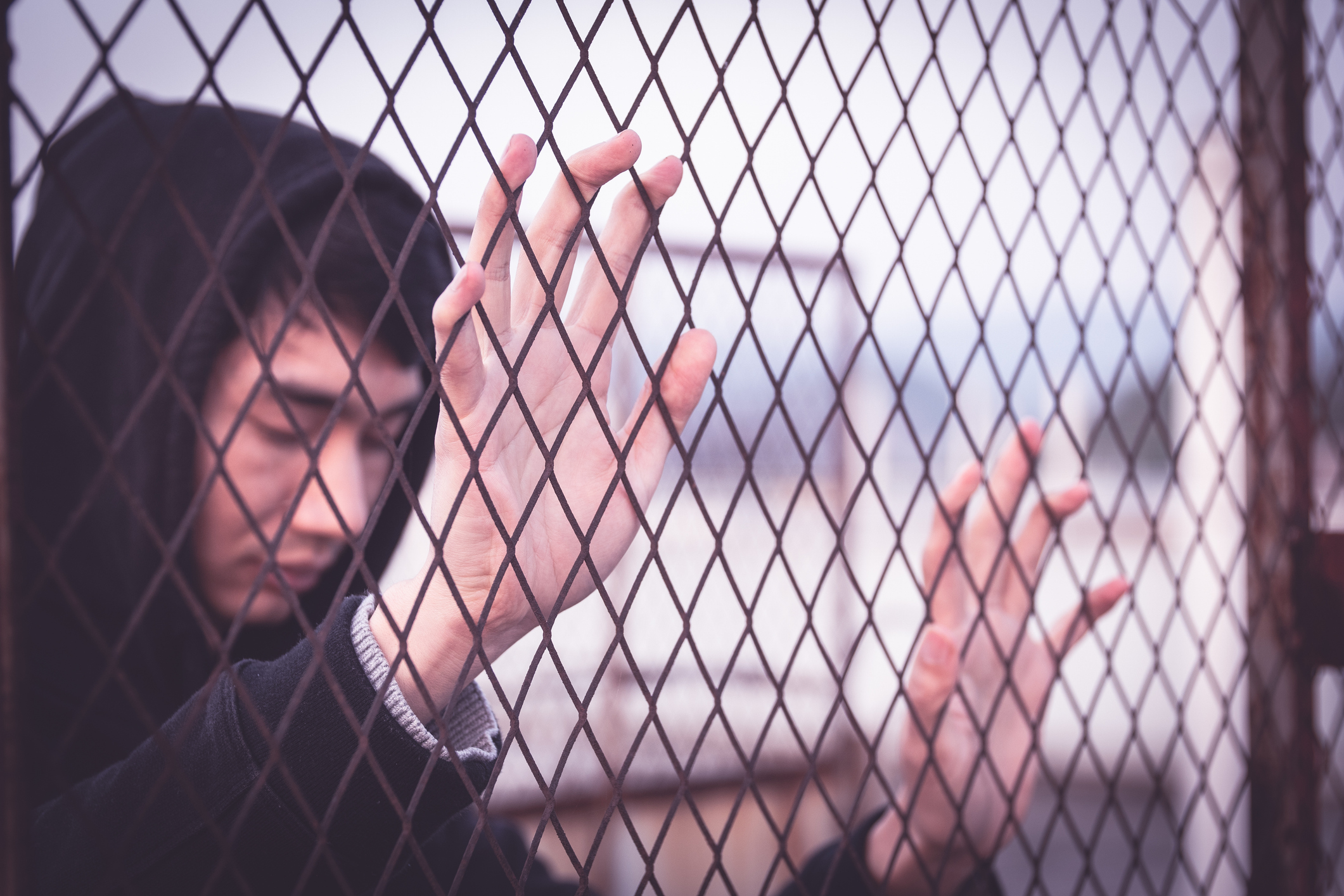 Young man wearing hoodie is detained behind a fence.