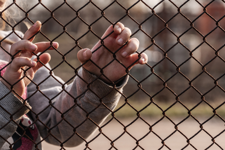 child's hands holding onto fence